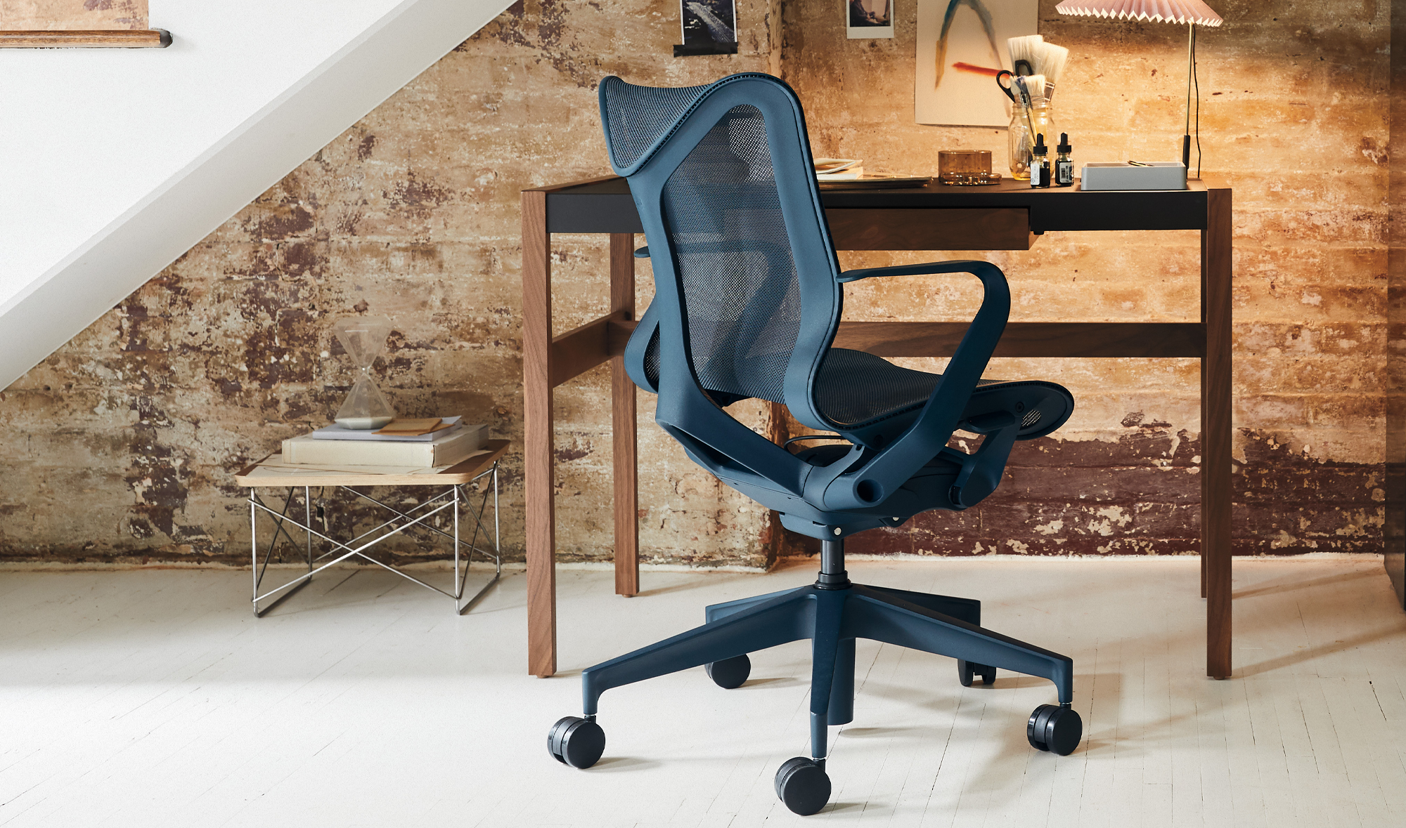 Un fauteuil de bureau Herman Miller Cosm bleu placé devant un bureau et sous un escalier dans un environnement domestique.