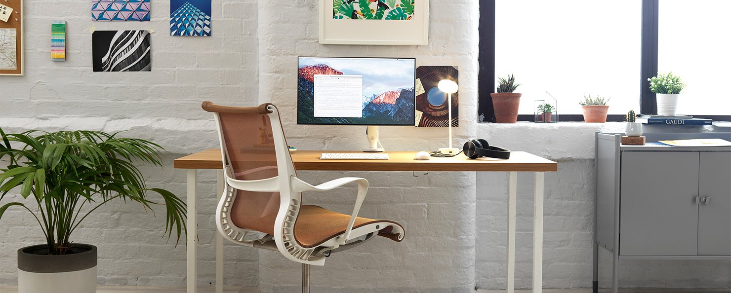 Single Ollin monitor arm on an office desk alongside an orange Setu chair