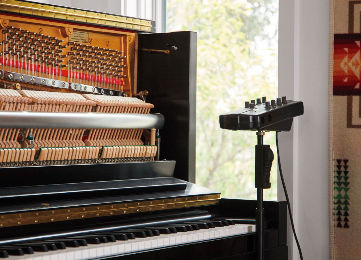 Photo d'un piano droit ouvert à l'avant, avec du matériel d'enregistrement à côté